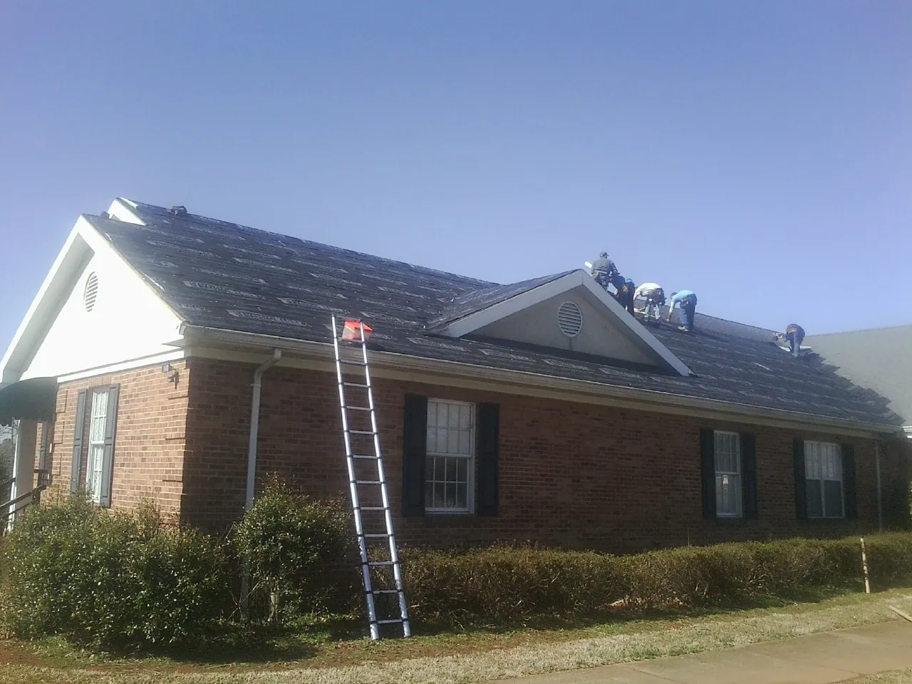 Crew tearing shingles off a brick ranch roof with a ladder set — Metal Roof Repair work by our crew in Milroy