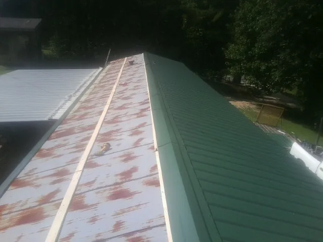 Old rusted panels beside newly installed green metal roofing — Wind Damage Roof Repair by Roofing Brothers in Milroy