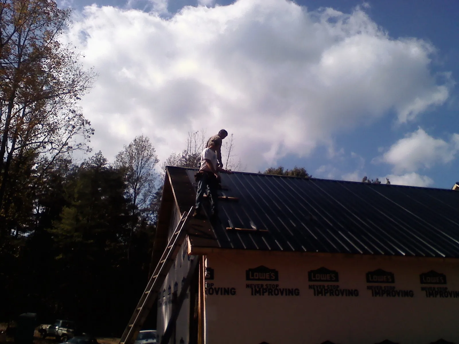 Roofer fastening dark metal panels high against a cloudy sky, from a Roof Inspection job in Milroy
