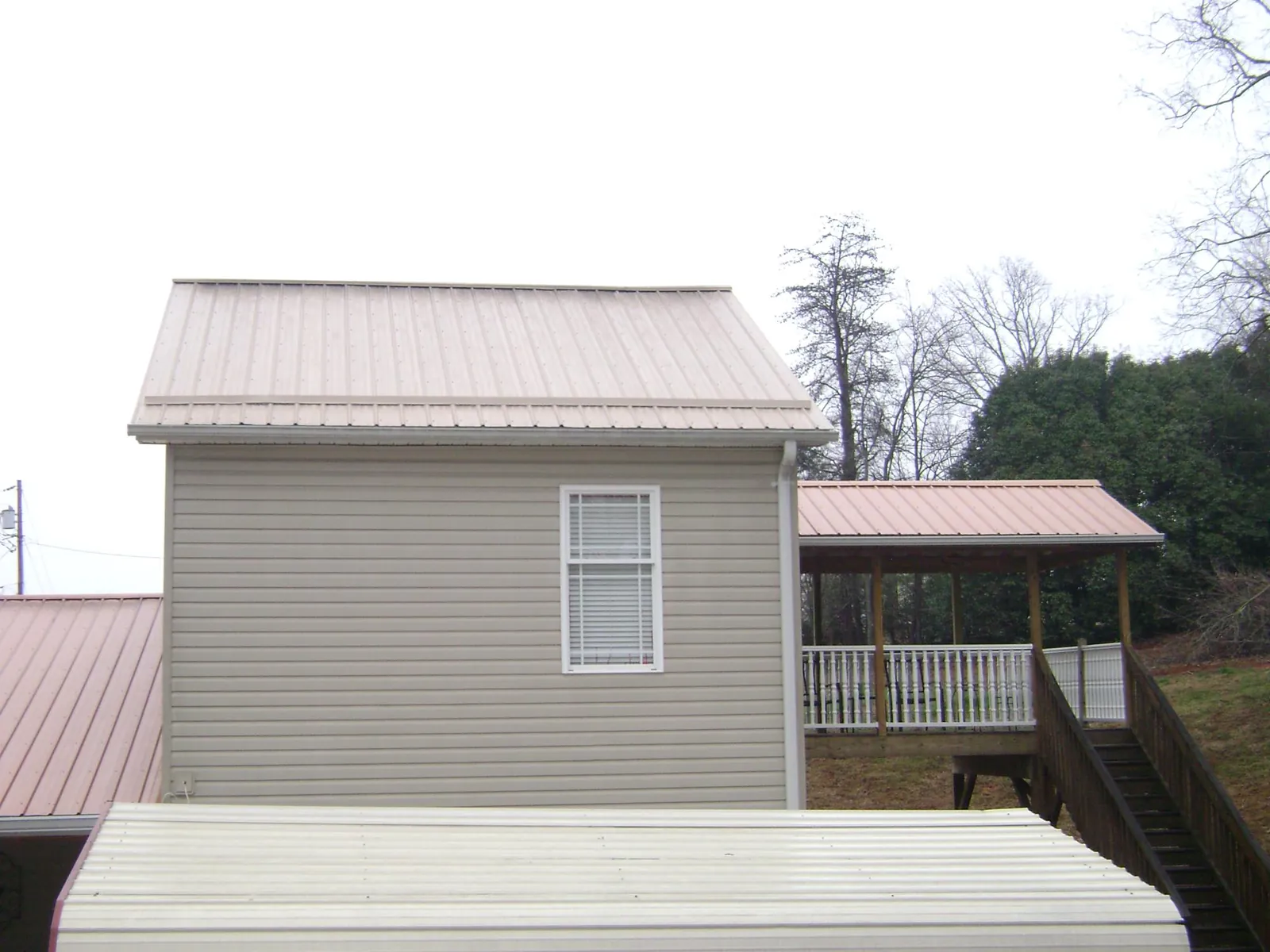 Tan metal roofs on a two story addition and attached porch, from a Roof Replacement job in Milroy